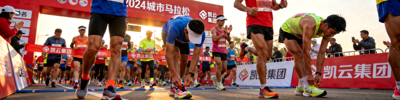 2024城市马拉松起跑现场，众多参赛者身着运动服在起点线前准备出发，背景有凯云集团冠名标识